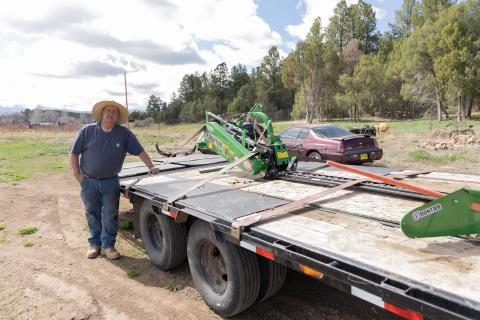 man stands next to hay cutting equipment