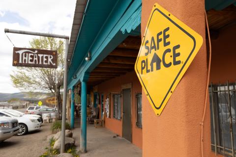 A building with a Theater sign hanging on the left and a safe place sign on a pole on the right