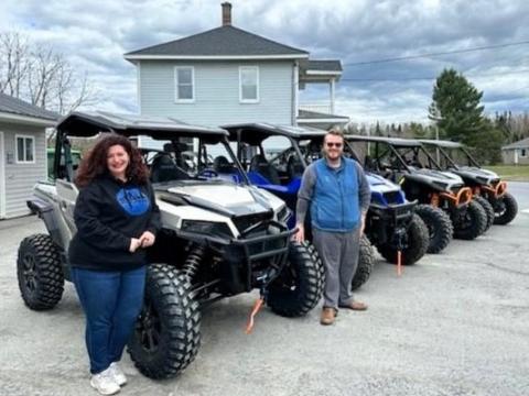 A woman and man stand in front of a line of ATVs in a parking lot under gray skies.
