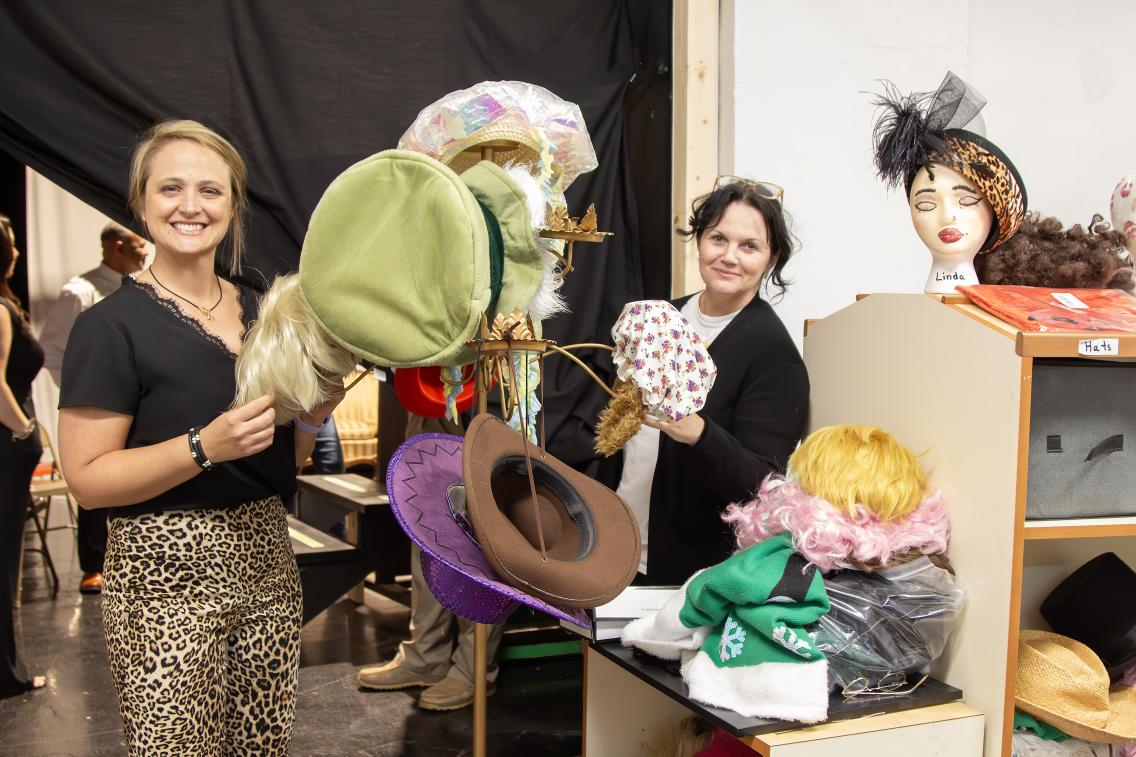 Jessica Savage and Brandee Brown display some of the wigs and hats stored backstage at the CAM.