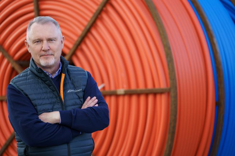 man looking at camera in front of spool of fiber
