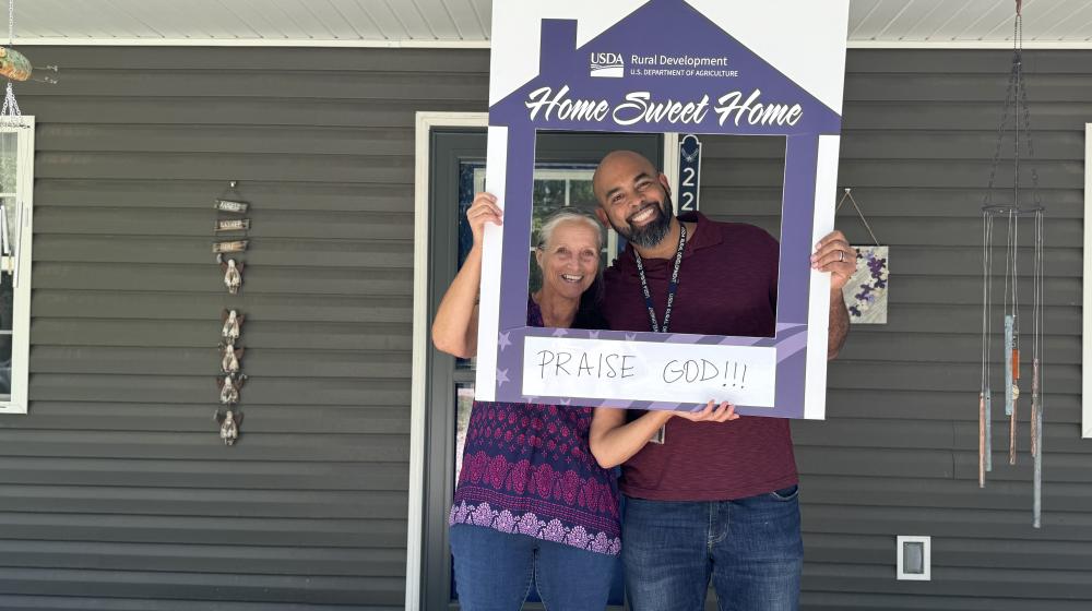 Ariel and Mike holding a home sweet home picture frame in front of Ariel's home