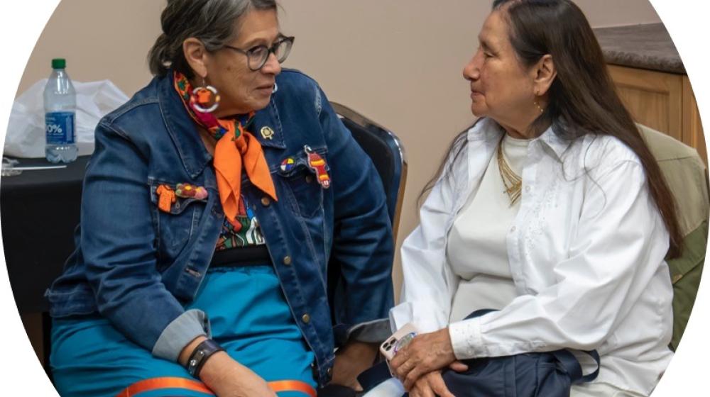 Native American ladies sitting in chairs, talking and smiling with each other.