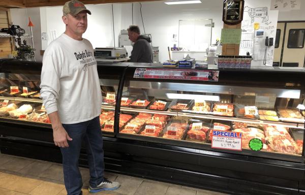 Randy Gruenwald standing in front of a display of meats.