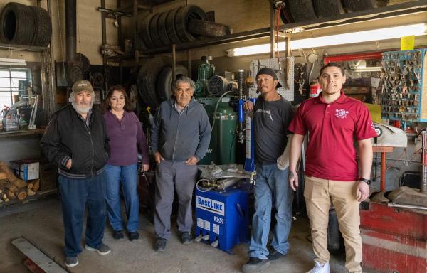 Five people pose for a photo in a tire shop garage area