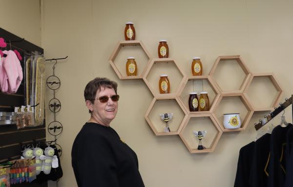 Smiling woman standing in a shop with honey and honey-themed products on shelves on the walls and on racks.